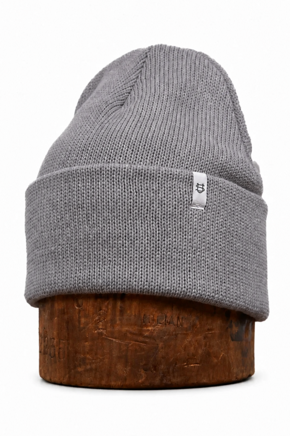 A gray ribbed knit beanie hat displayed on a brown wooden stand against a plain white background.