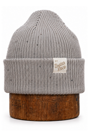 A light gray speckled knit beanie hat with a folded cuff and a small white brand patch reading 'Upstate Stock', displayed on a brown wooden stand against a white background.