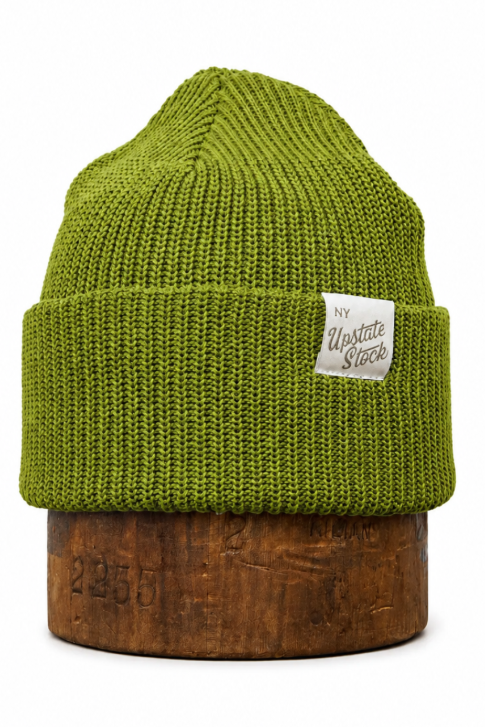 An olive green ribbed knit beanie hat with a small white 'My Outside Stuff' brand label on the side, displayed on a rustic wooden block against a white background.