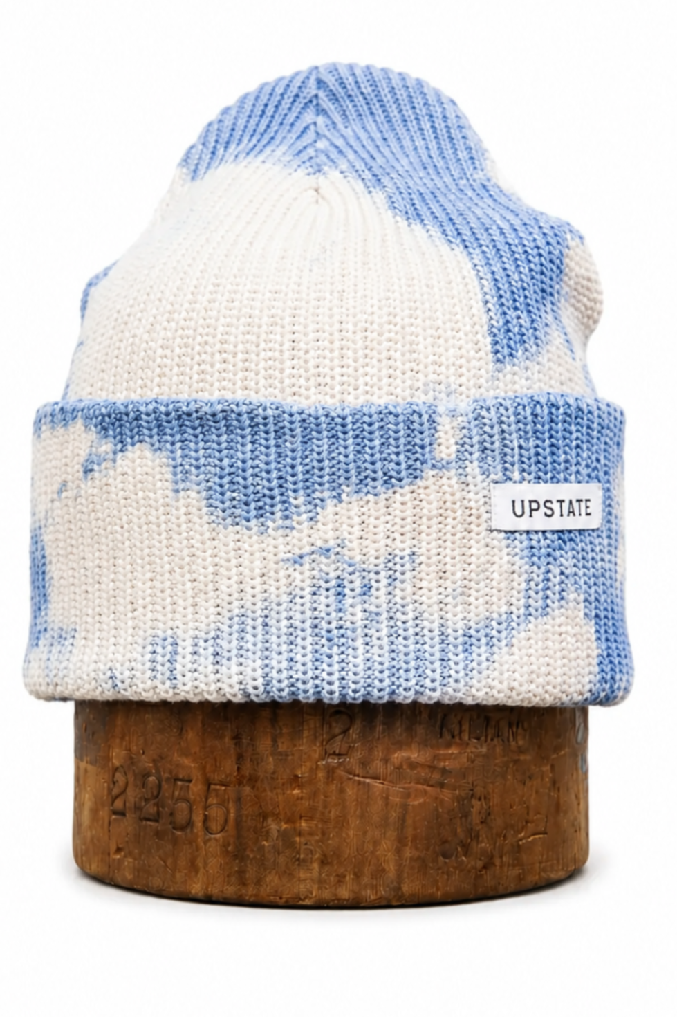 A knit beanie hat with a blue and off-white cloud pattern, displayed on a wooden stand against a white background. A small white label on the cuff reads 'UPSTATE'.