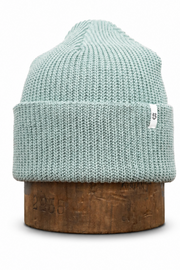A light mint green ribbed knit beanie hat displayed on a round wooden stand against a plain white background.
