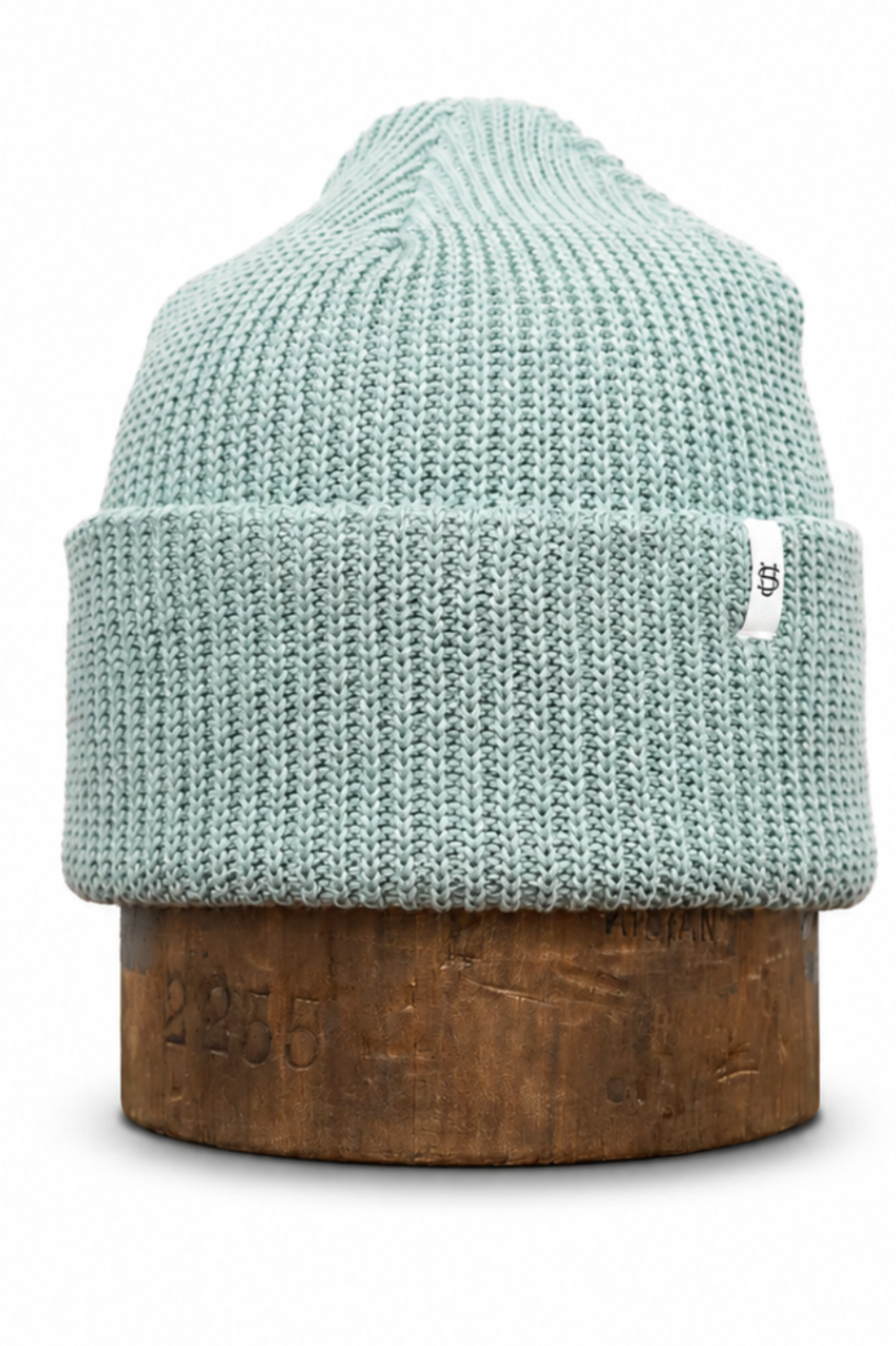 A light mint green ribbed knit beanie hat displayed on a round wooden stand against a plain white background.