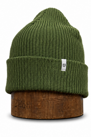 An olive green ribbed knit beanie hat displayed on a brown wooden stand against a plain white background.