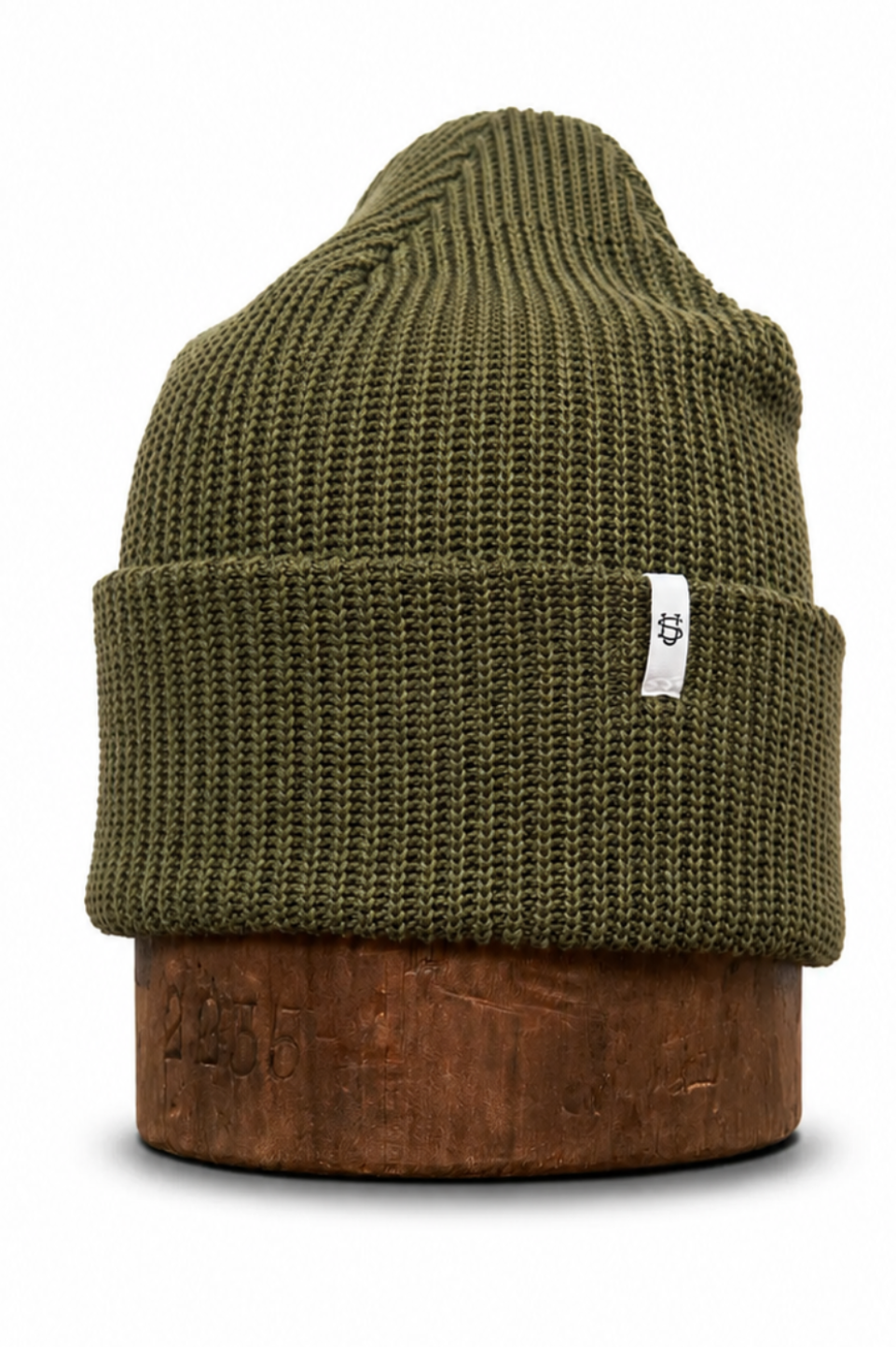 An olive green ribbed knit beanie hat displayed on a brown wooden block against a white background.