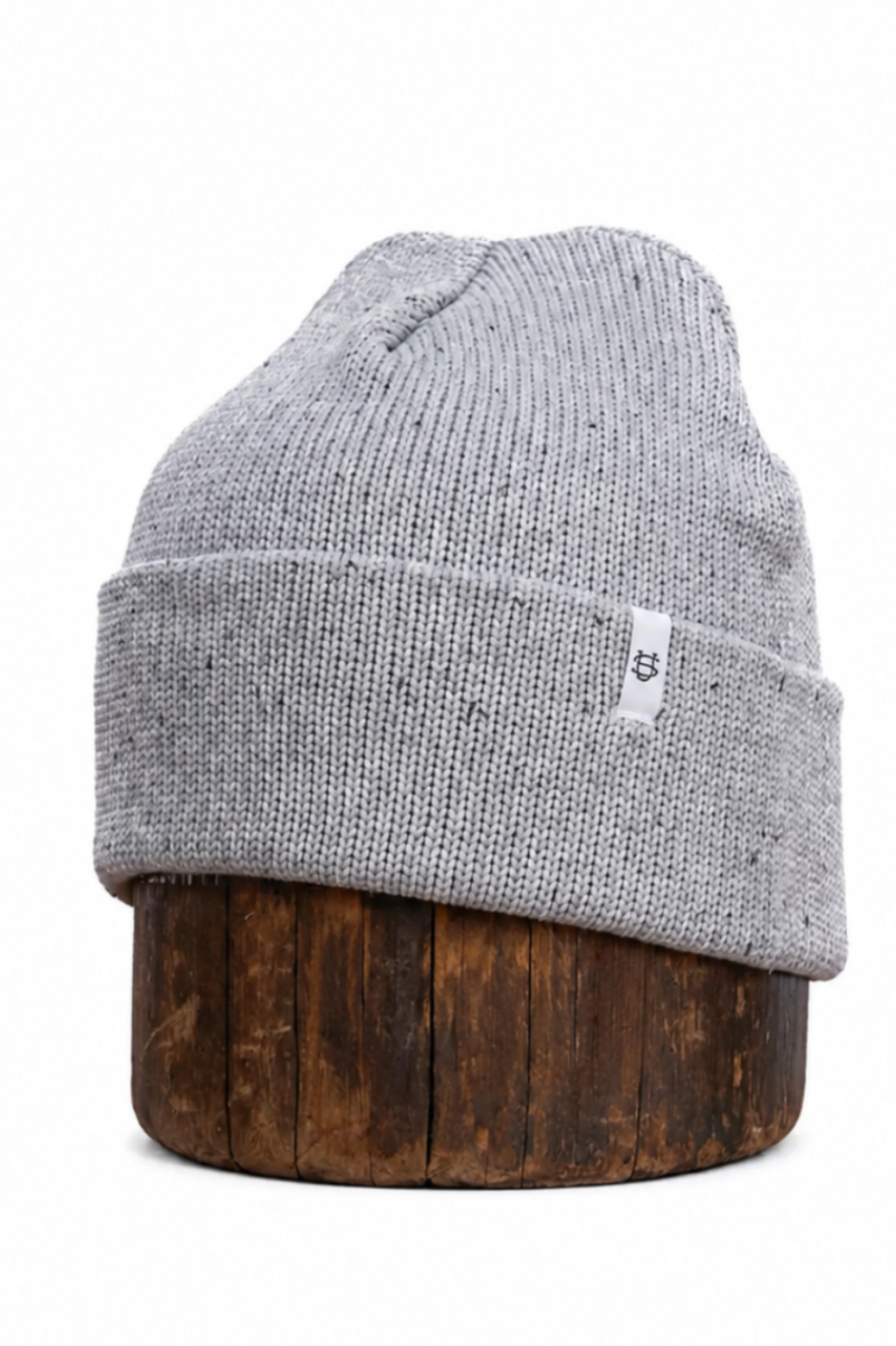 A light gray heathered knit beanie hat with a small white tag, displayed on a dark brown wooden stand against a plain white background.