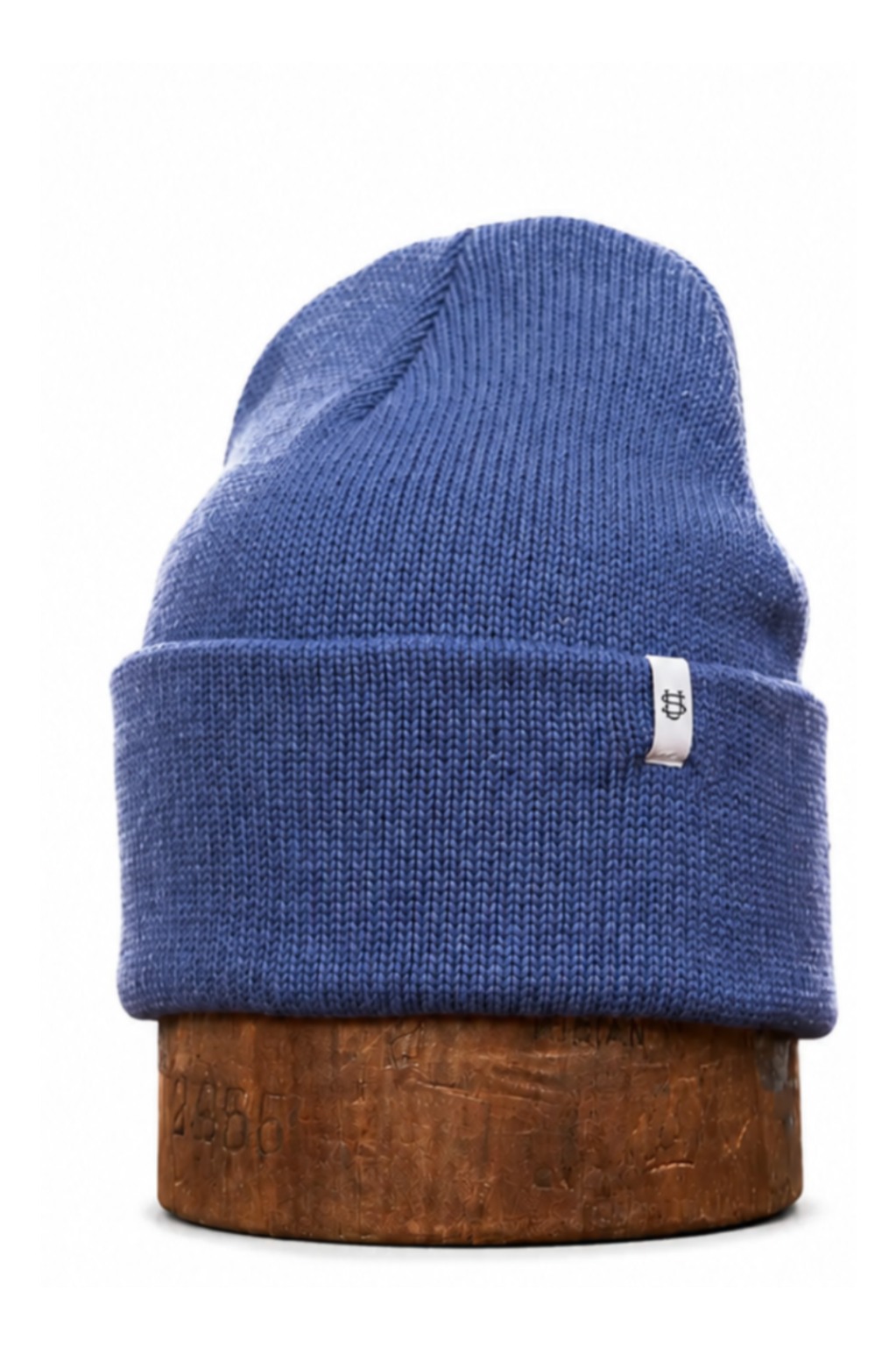 A blue ribbed knit beanie hat displayed upright on a round wooden block against a plain white background.