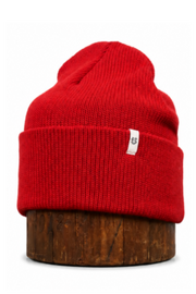 A bright red ribbed knit beanie hat displayed on a round wooden stand against a plain white background.