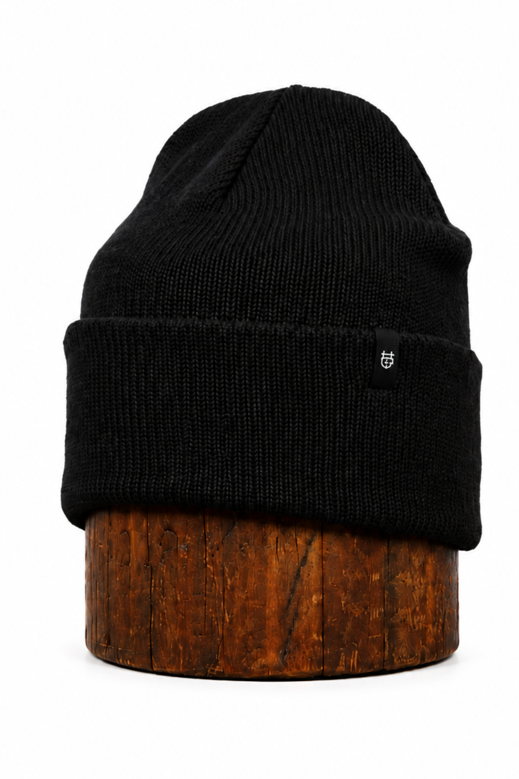 A black ribbed knit beanie hat displayed on a brown wooden stand against a plain white background.