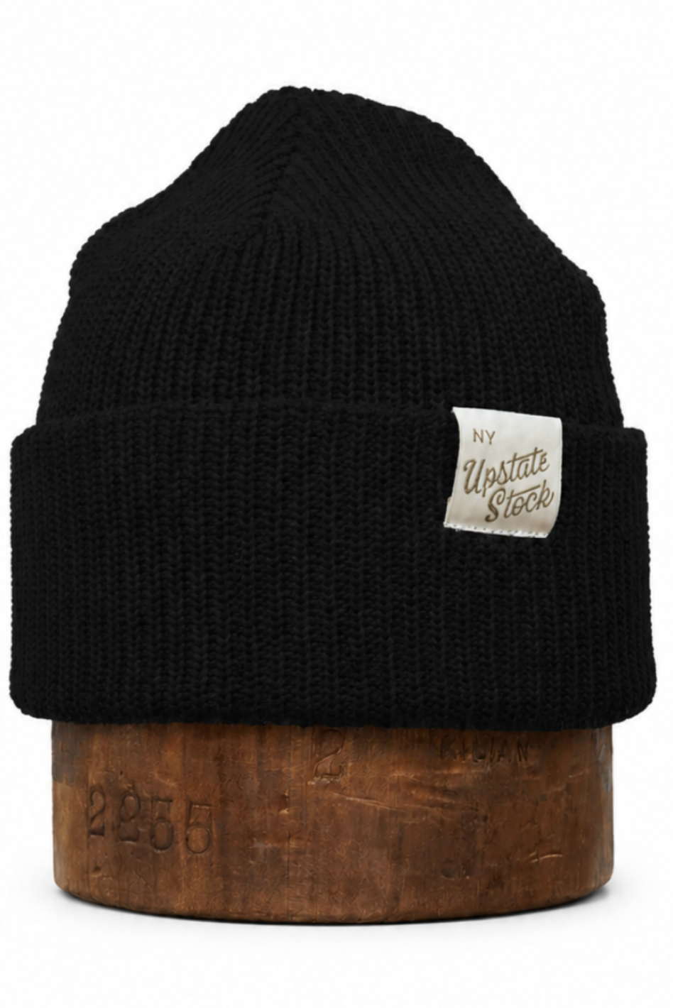 A black ribbed knit beanie hat with a small white rectangular patch reading 'The Western Store' on the side, displayed on a brown wooden stand against a plain white background.