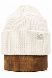 An off-white ribbed knit beanie hat displayed on a wooden stand against a plain white background. A small woven label on the cuff reads 'New York Vintage Store'.