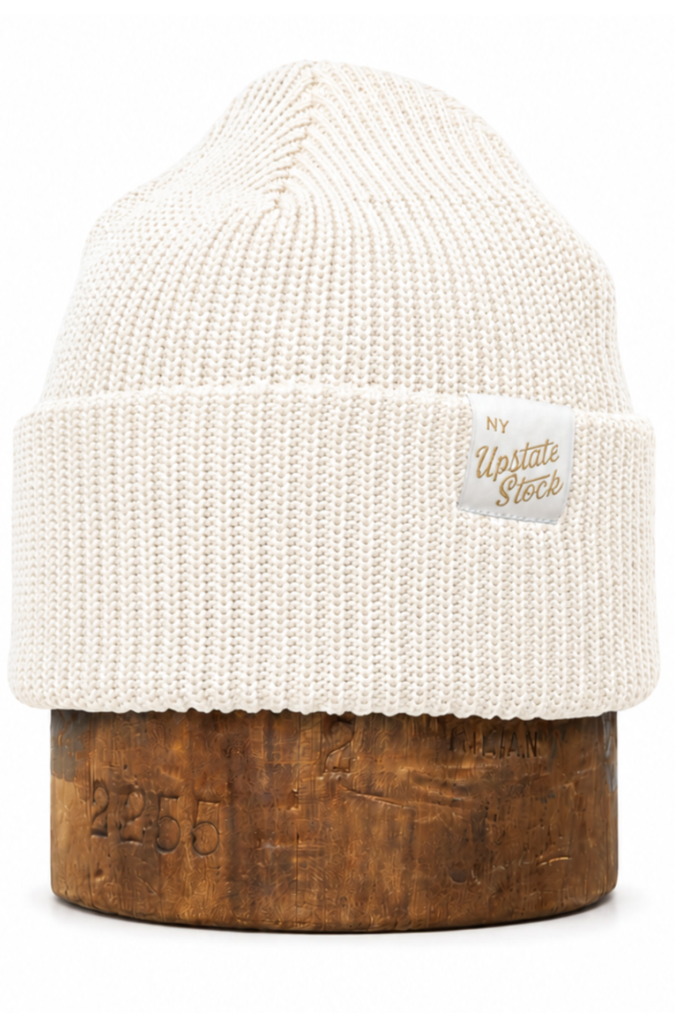 An off-white ribbed knit beanie hat displayed on a wooden stand against a plain white background. A small woven label on the cuff reads 'New York Vintage Store'.