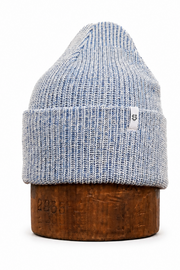 A light blue and white heathered knit beanie hat displayed on a round wooden stand against a plain white background.