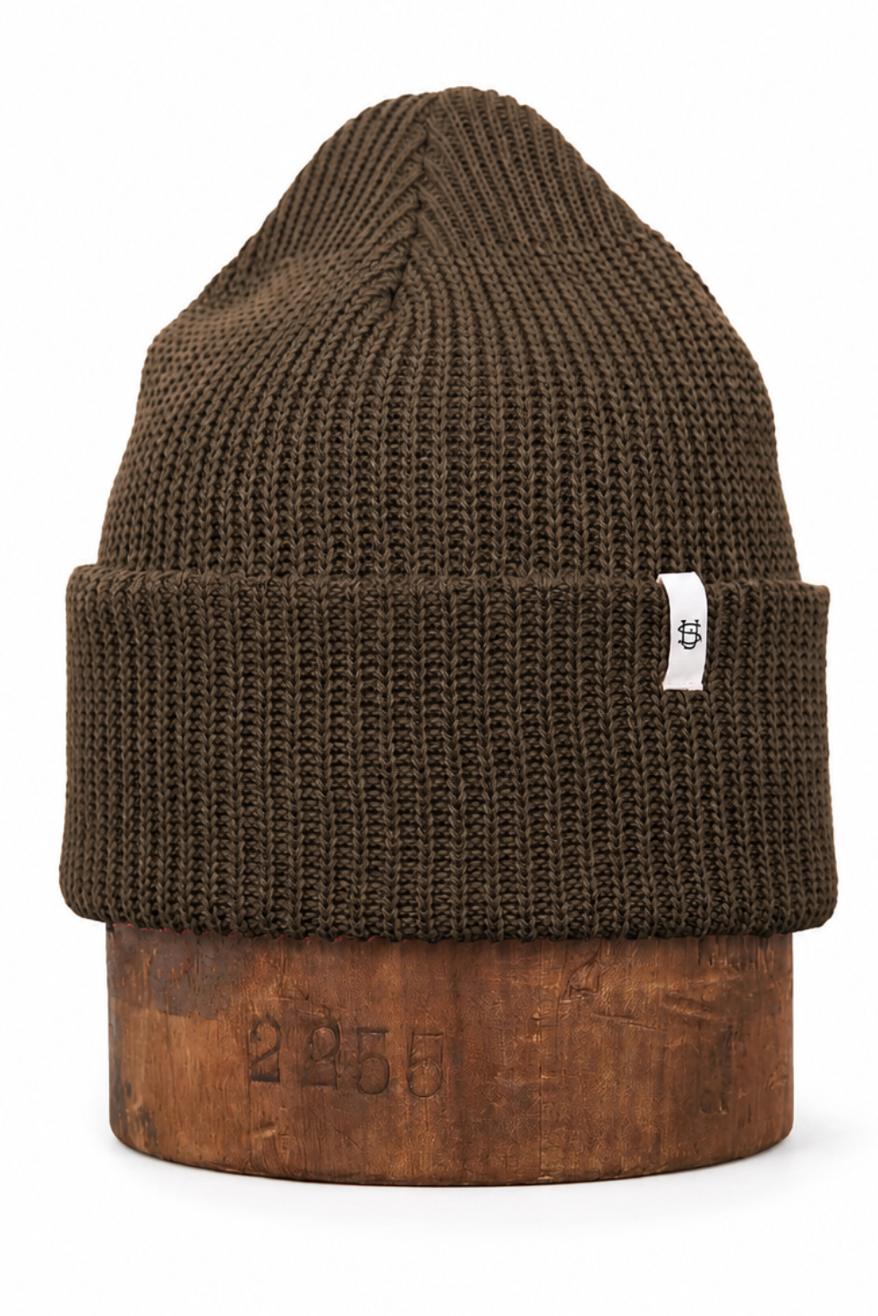 A dark brown ribbed knit beanie hat with a folded cuff, displayed on a wooden block against a white background.