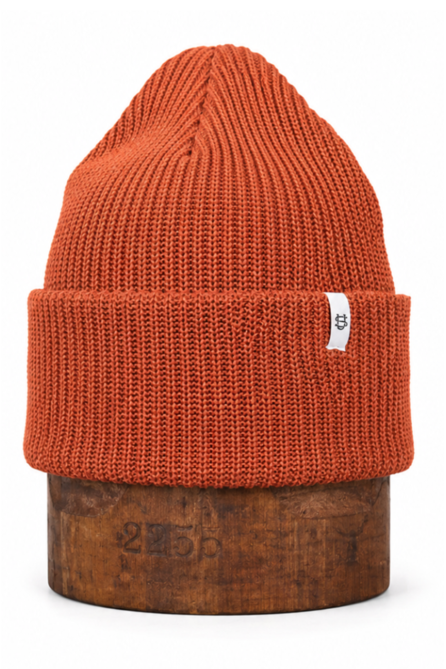 An orange ribbed knit beanie hat displayed on a wooden stand against a plain white background.