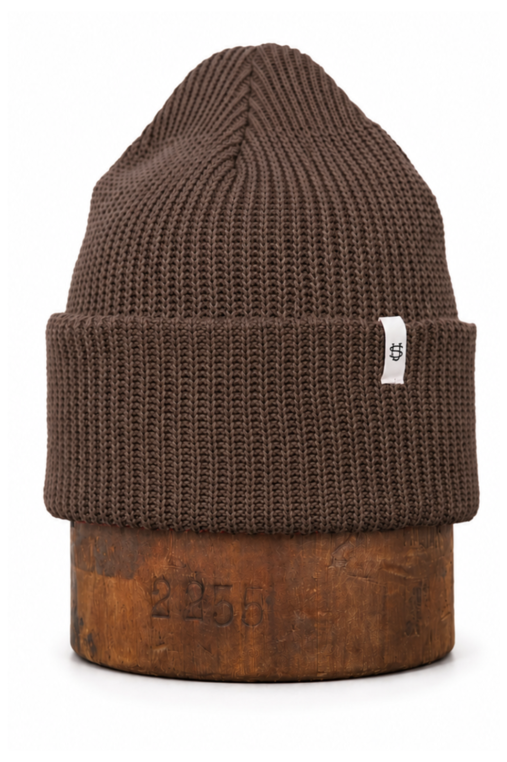 A brown ribbed knit beanie hat with a folded cuff, displayed on a rustic wooden block against a plain white background.