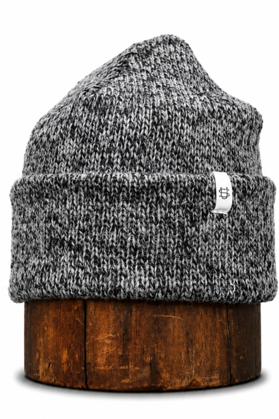 A gray and black marled knit beanie hat with a small white brand tag, displayed on a round wooden stand against a white background.