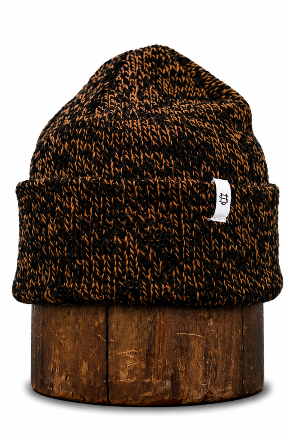 A brown and black marled knit beanie hat with a small white brand tag, displayed on a rustic wooden stand against a white background.