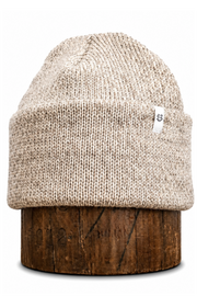 A beige knit beanie hat displayed on a dark brown wooden stand against a plain white background.