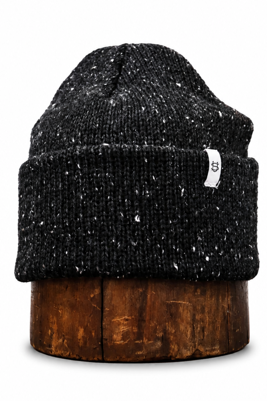 A black and white speckled knit beanie hat displayed on a brown wooden stand against a plain white background.