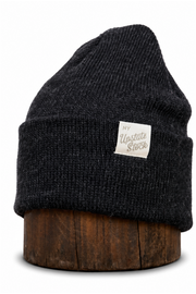 A dark charcoal gray ribbed knit beanie hat with a small white rectangular patch reading 'My Upstate Stock', displayed on a round wooden stand against a white background.