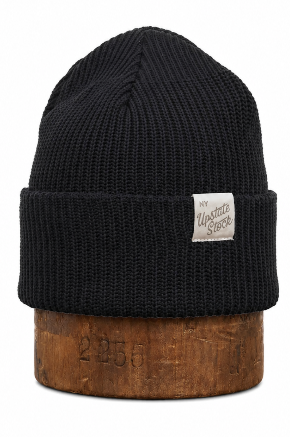 A black ribbed knit beanie hat with a small white 'Western Store' brand patch on the front cuff, displayed on a rustic wooden block against a white background.