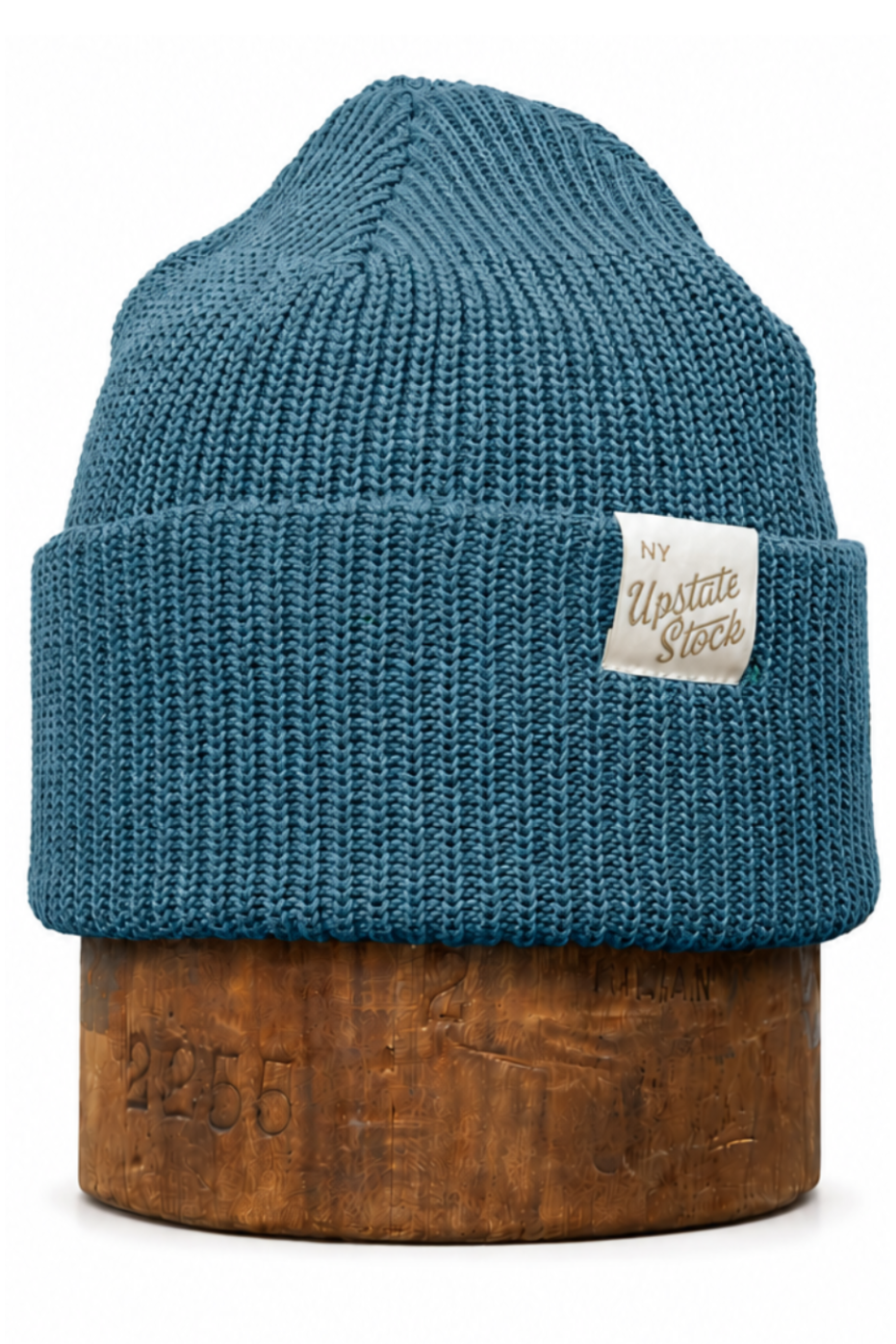 A teal blue ribbed knit beanie hat with a folded cuff, displayed on a wooden stand against a plain white background. A small white woven label on the cuff features the text 'The Misfits Society'.