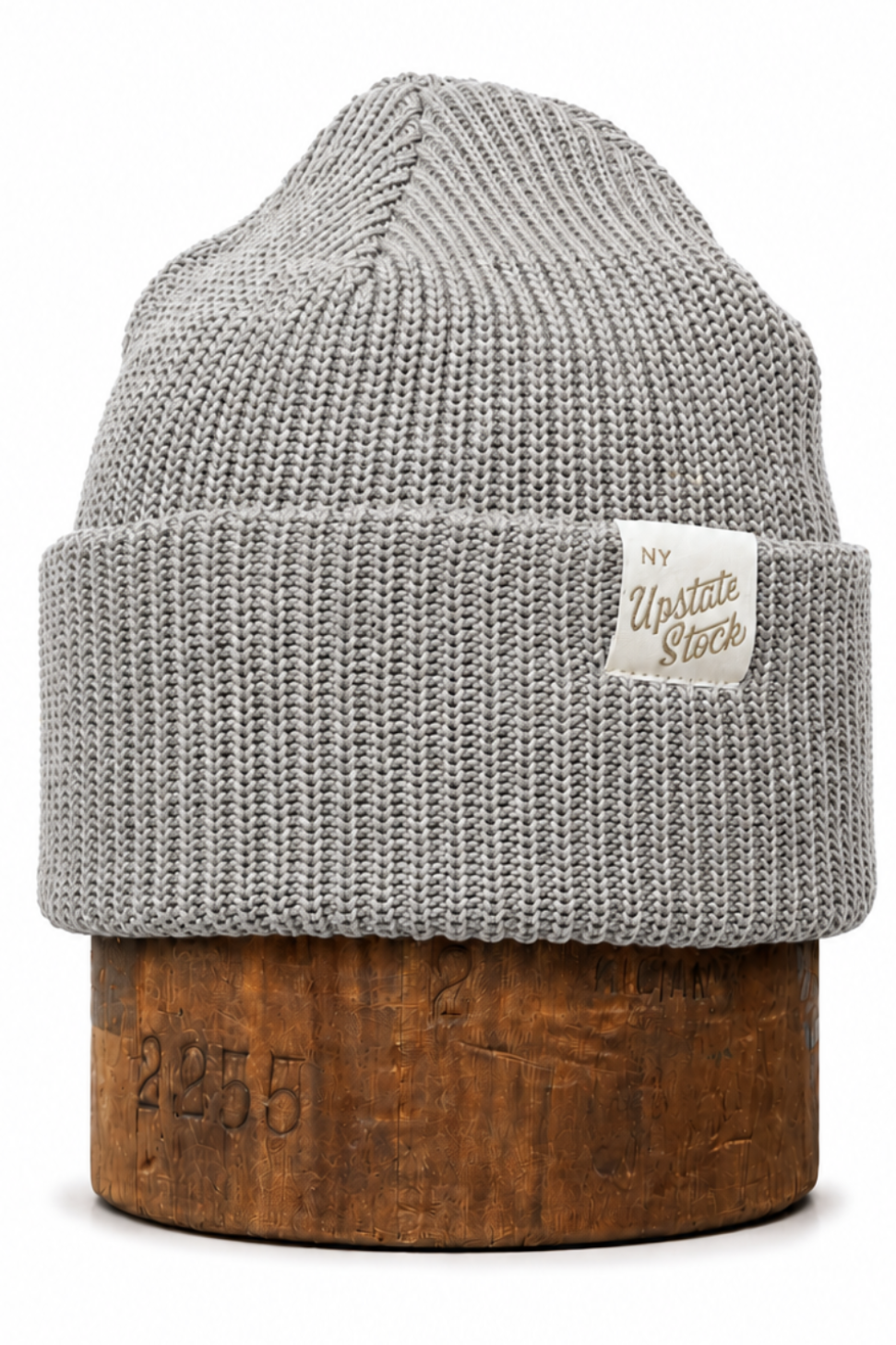 A light gray ribbed knit beanie hat with a folded cuff, displayed on a rustic wooden block against a clean white background. A small cream-colored brand tag reading 'My Update Store' is sewn onto the cuff.