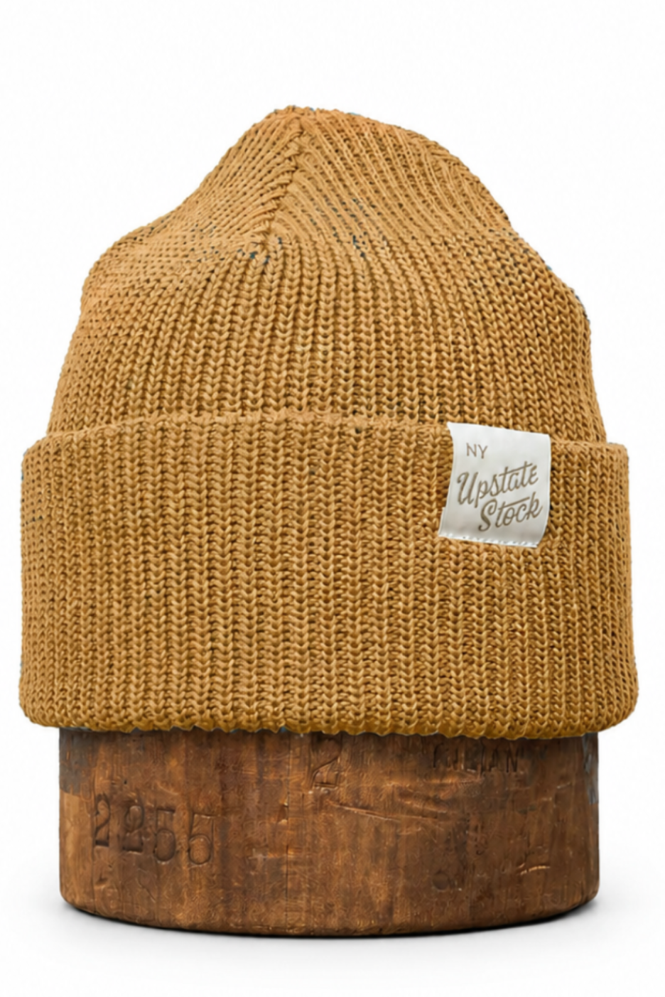 A mustard yellow ribbed knit beanie hat with a folded cuff, featuring a small white 'The Western Store' brand label on the side, displayed on a wooden stand against a white background.