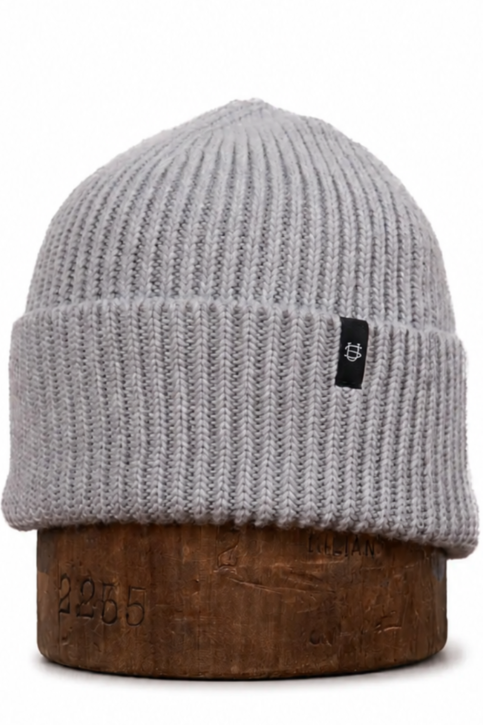 A light gray ribbed knit beanie hat displayed on a brown wooden stand against a plain white background.