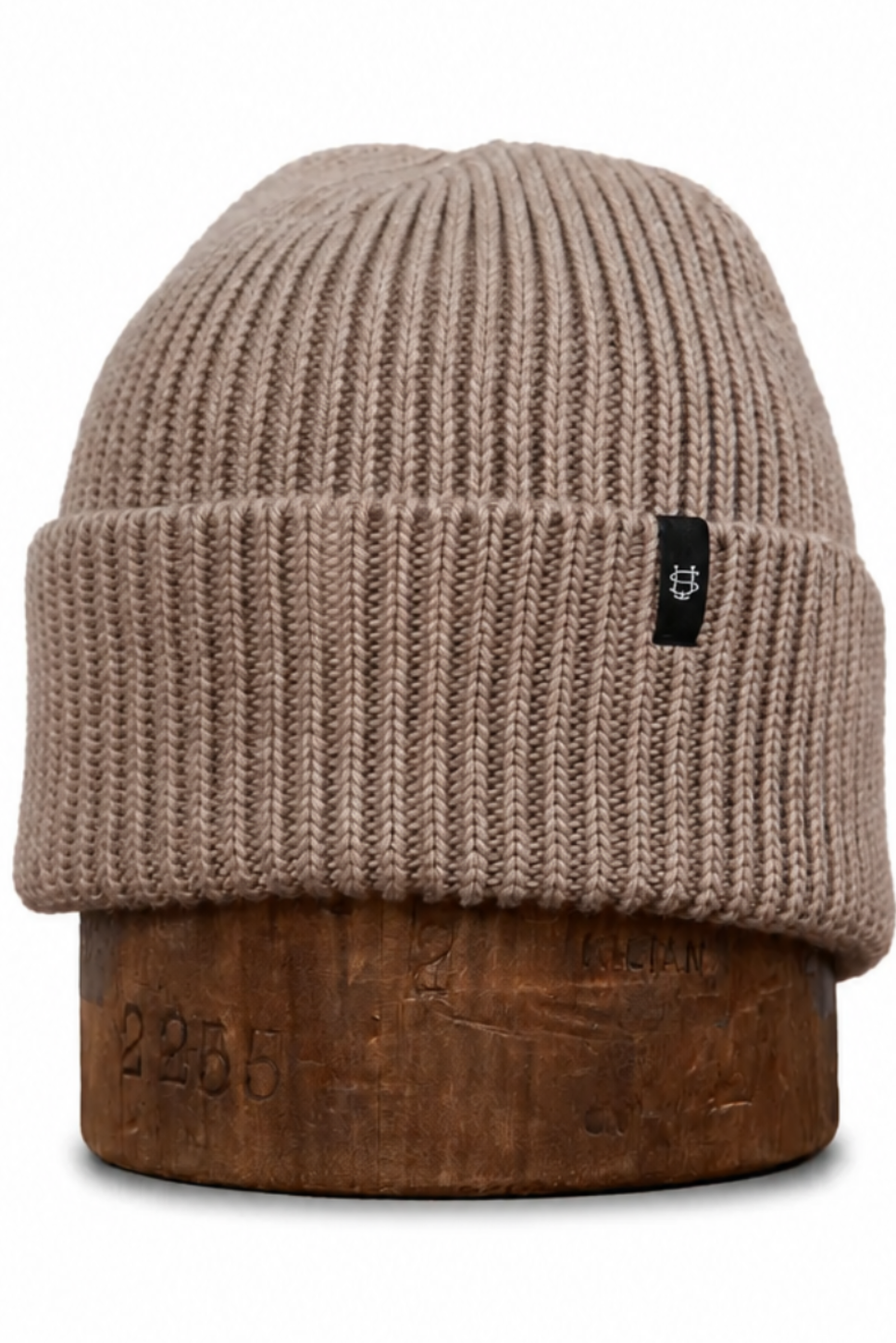 A ribbed knit beanie hat in a taupe-brown color, displayed on a wooden stand against a plain white background.