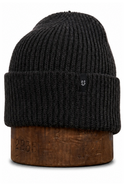 A black ribbed knit beanie hat displayed on a brown wooden stand against a plain white background.