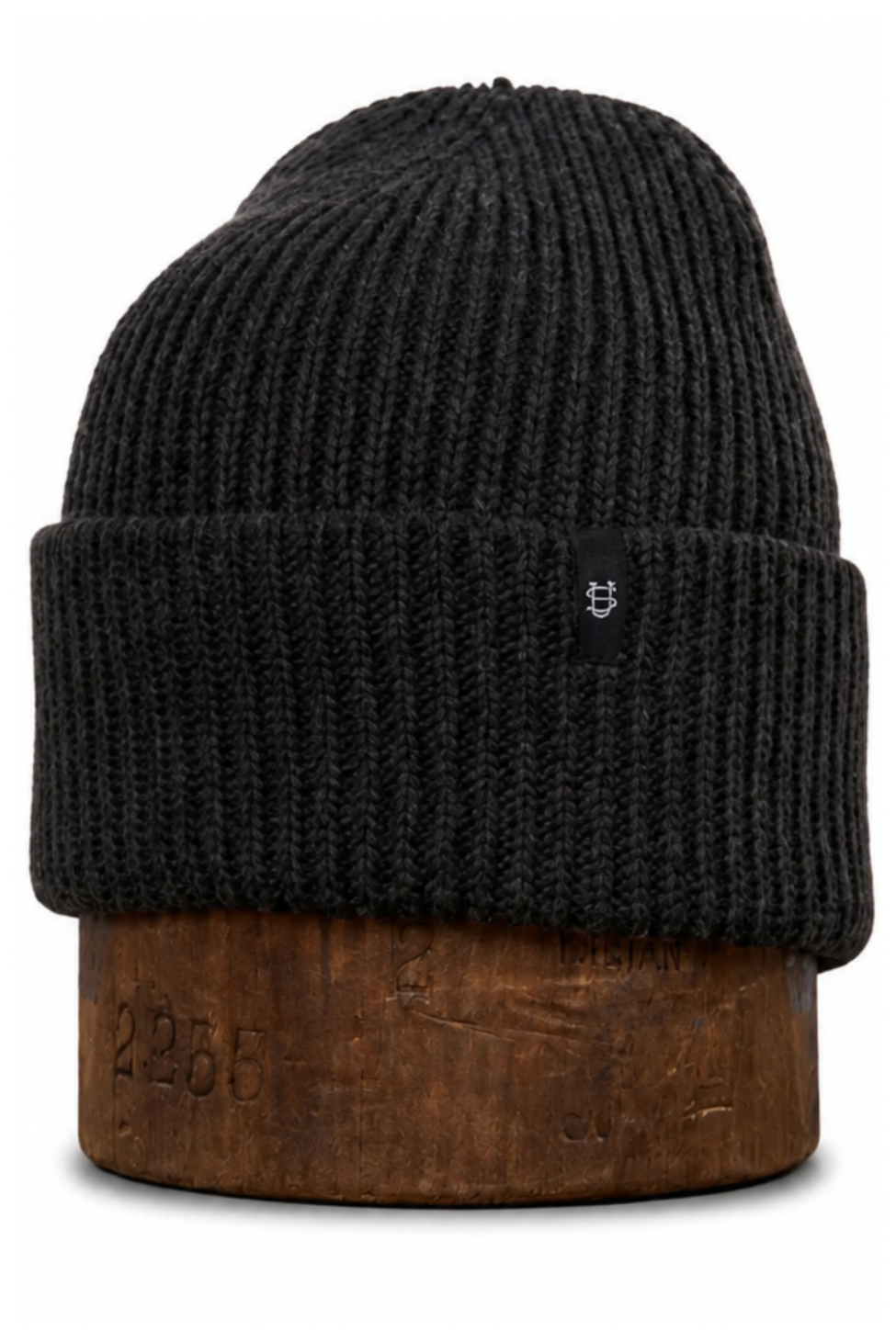 A black ribbed knit beanie hat displayed on a brown wooden stand against a plain white background.