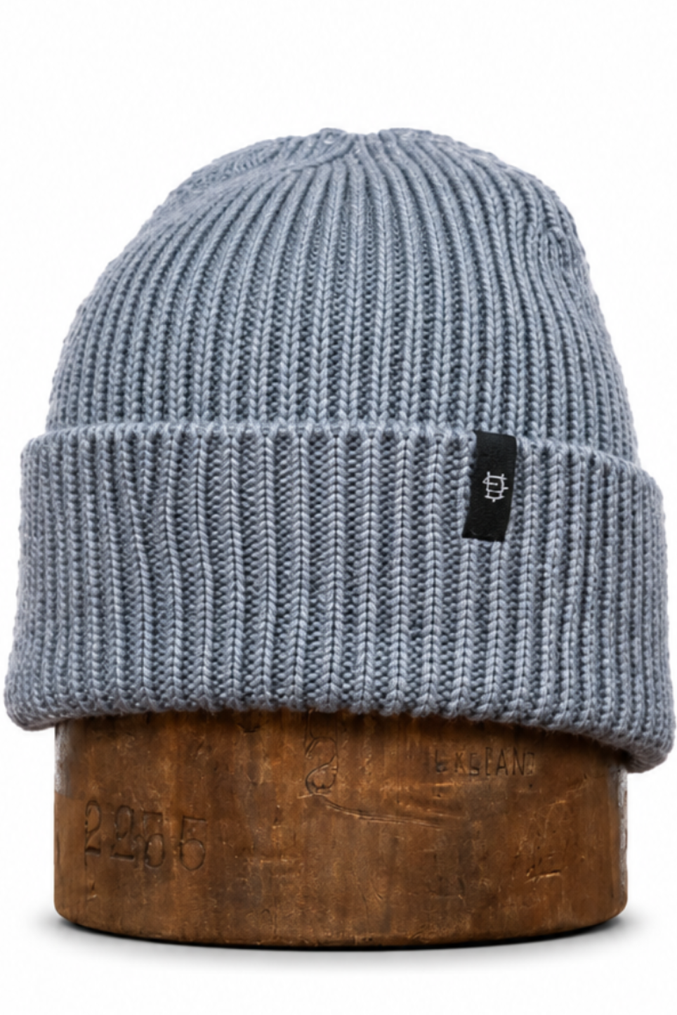 A light blue-gray ribbed knit beanie hat displayed on a wooden stand against a plain white background.