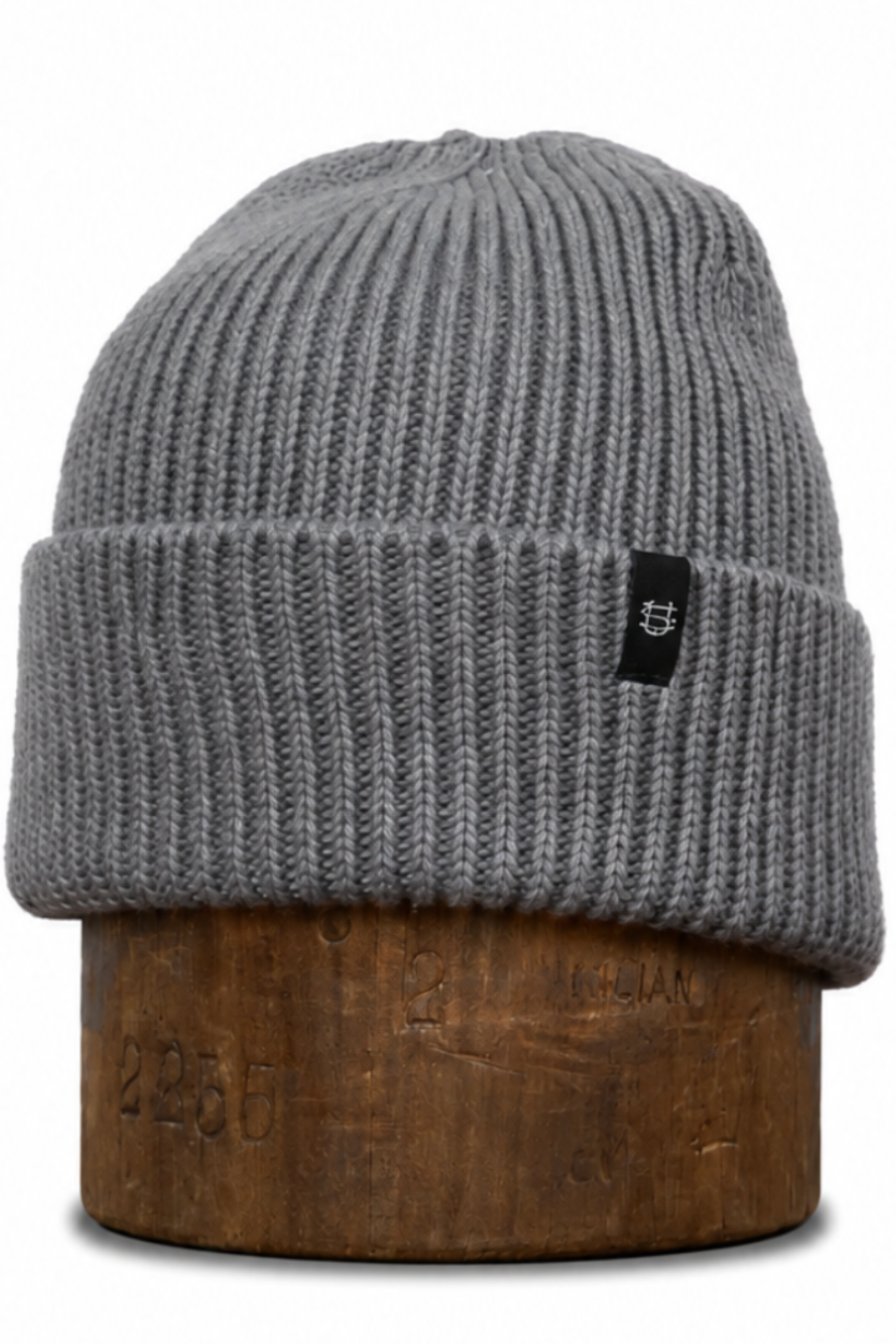 A gray ribbed knit beanie hat displayed on a brown wooden stand against a plain white background.