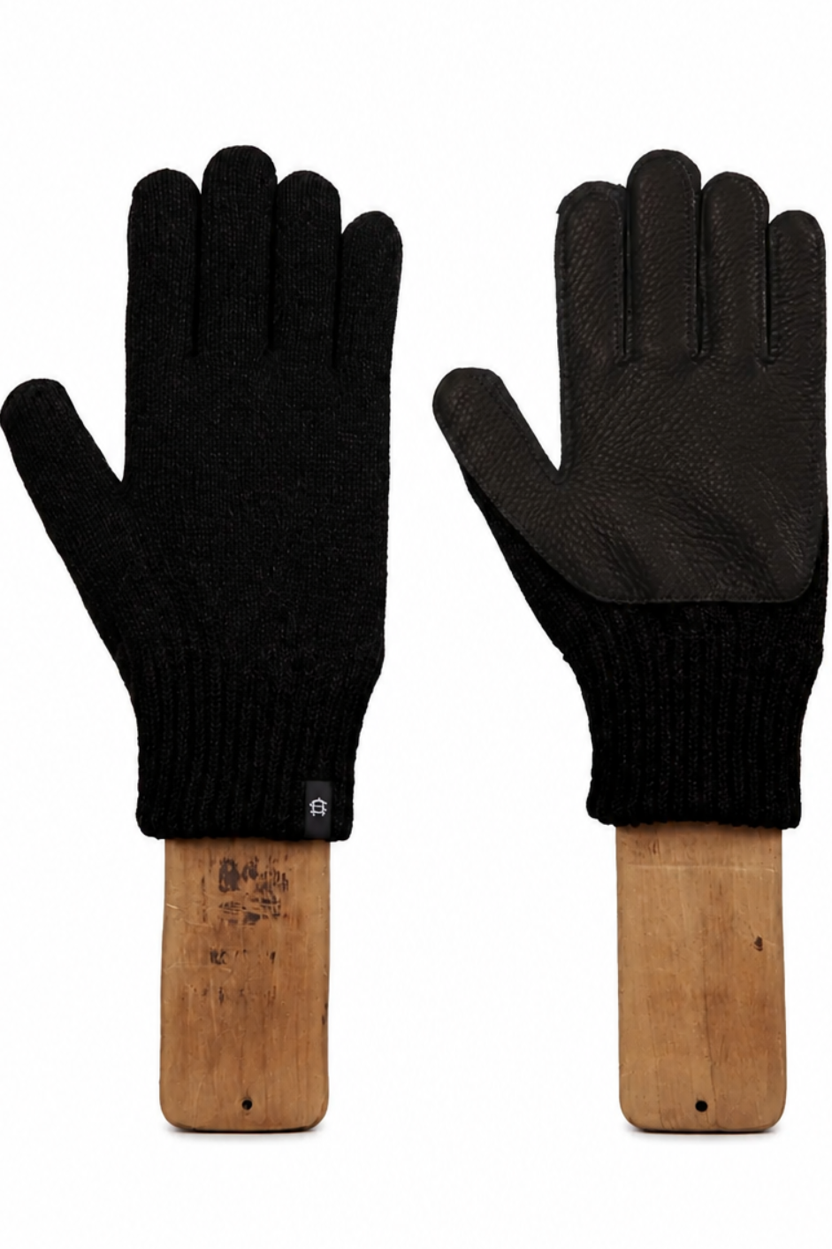 A pair of black knit gloves with dark brown leather palms, displayed on wooden handles against a white background.
