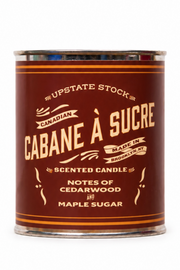 A single scented candle in a cylindrical metal tin with a dark brown label and cream lettering, reading 'Cabane à Sucré' and 'Notes of Cedarwood Maple Sugar' on a plain white background.