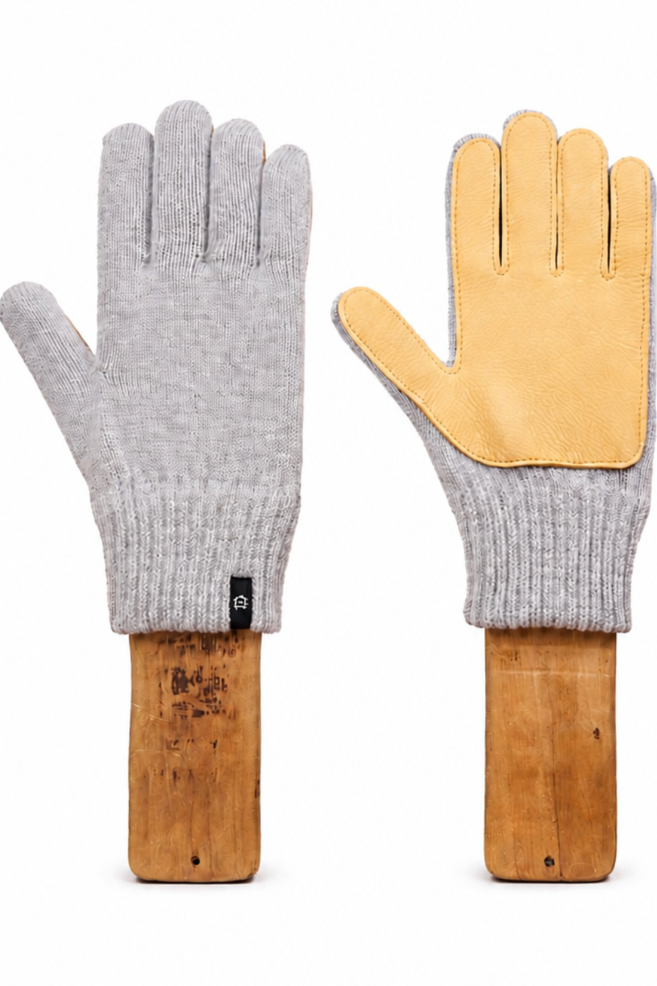 A pair of knit work gloves shown front and back on wooden handles against a white background. The left glove is shown from the back, featuring a light gray heather knit body with a tan leather back panel.