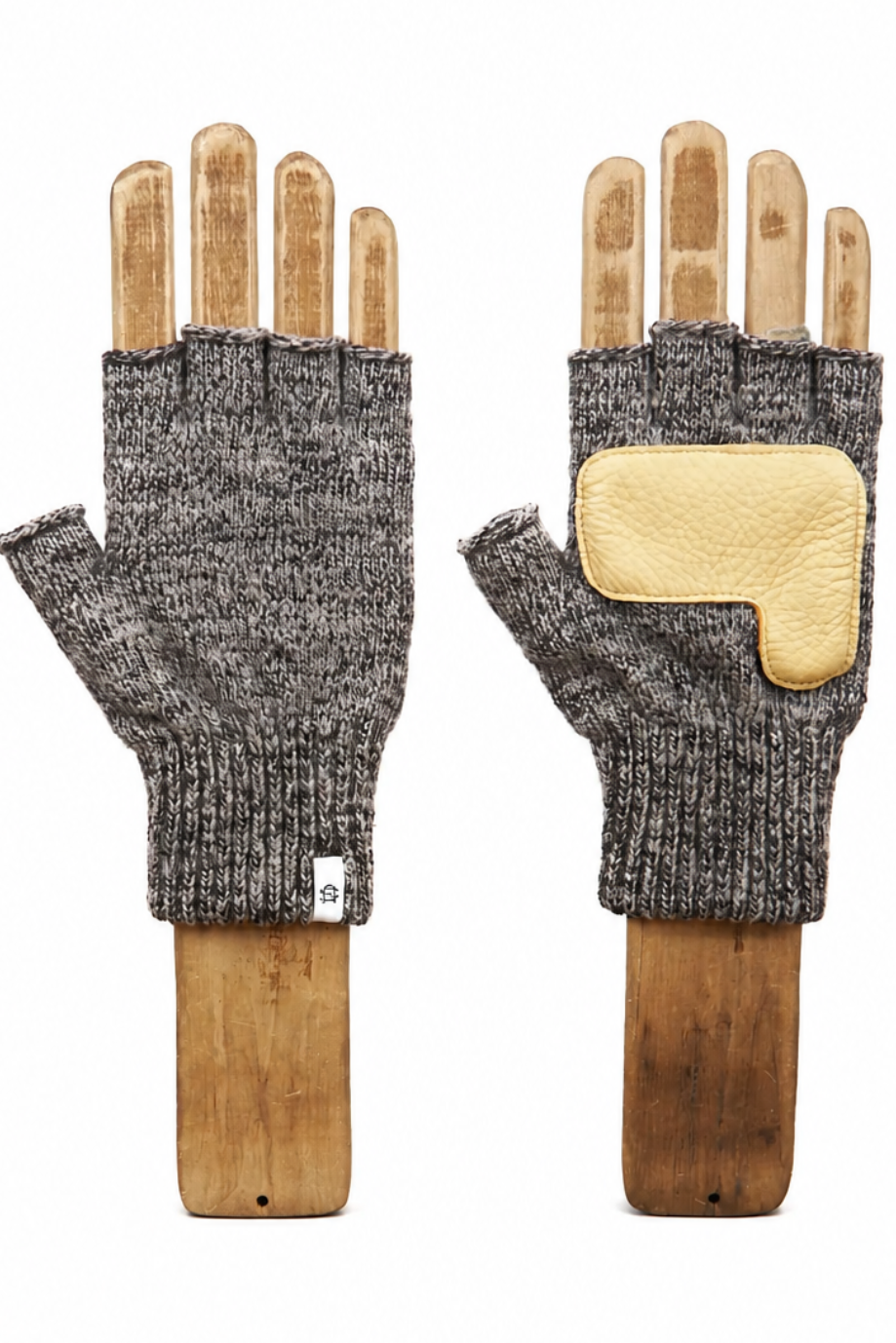 A pair of fingerless knit gloves displayed on wooden hand forms against a plain white background. The gloves are heather gray on the knit body with a contrasting light tan leather patch on the back of one glove.