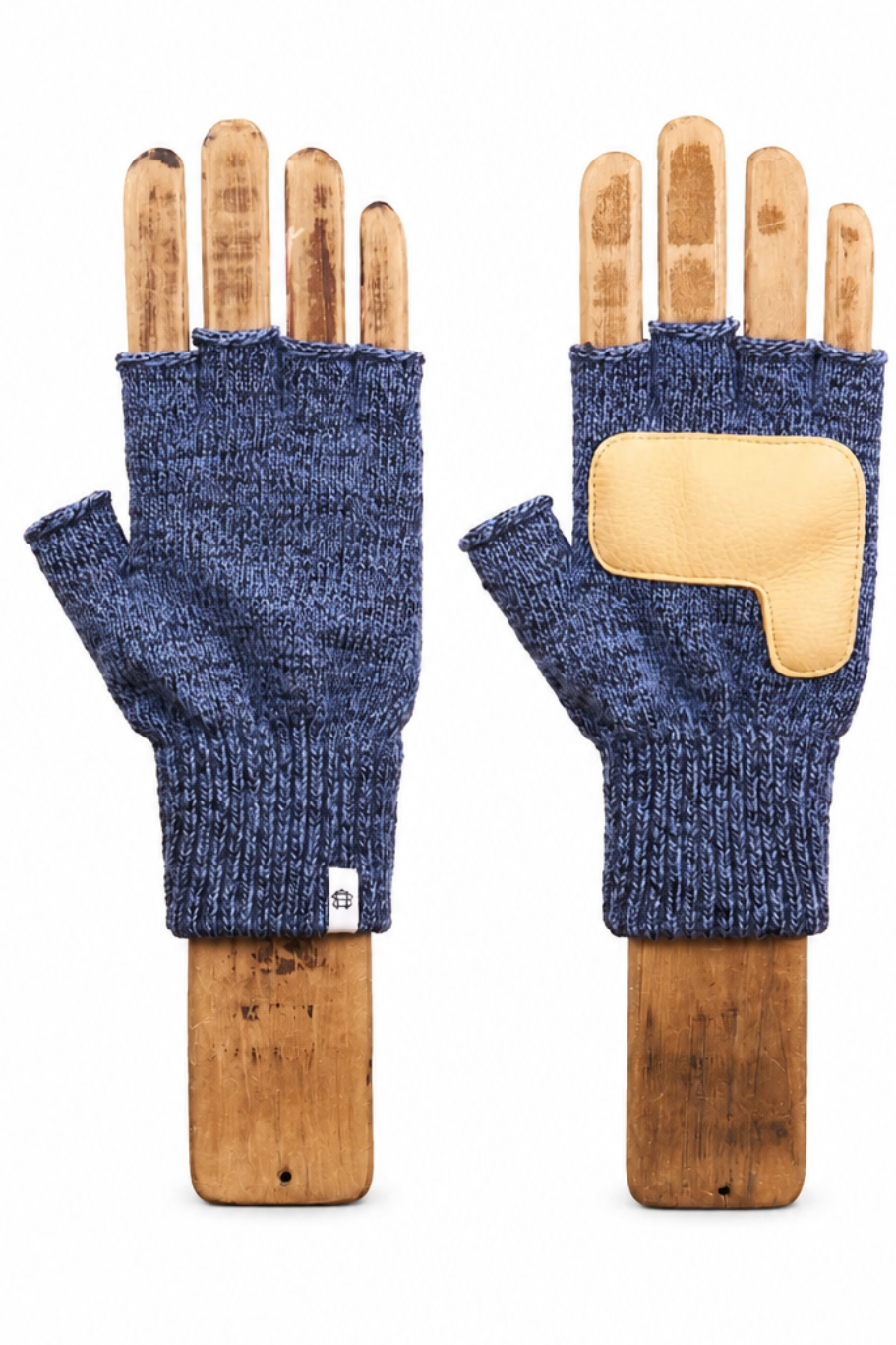 A pair of fingerless knit gloves in heathered navy blue, displayed on wooden hand forms against a plain white background. One glove shows the textured knit body and thumb cutout, while the other shows a beige suede or leather patch on the back of the hand.