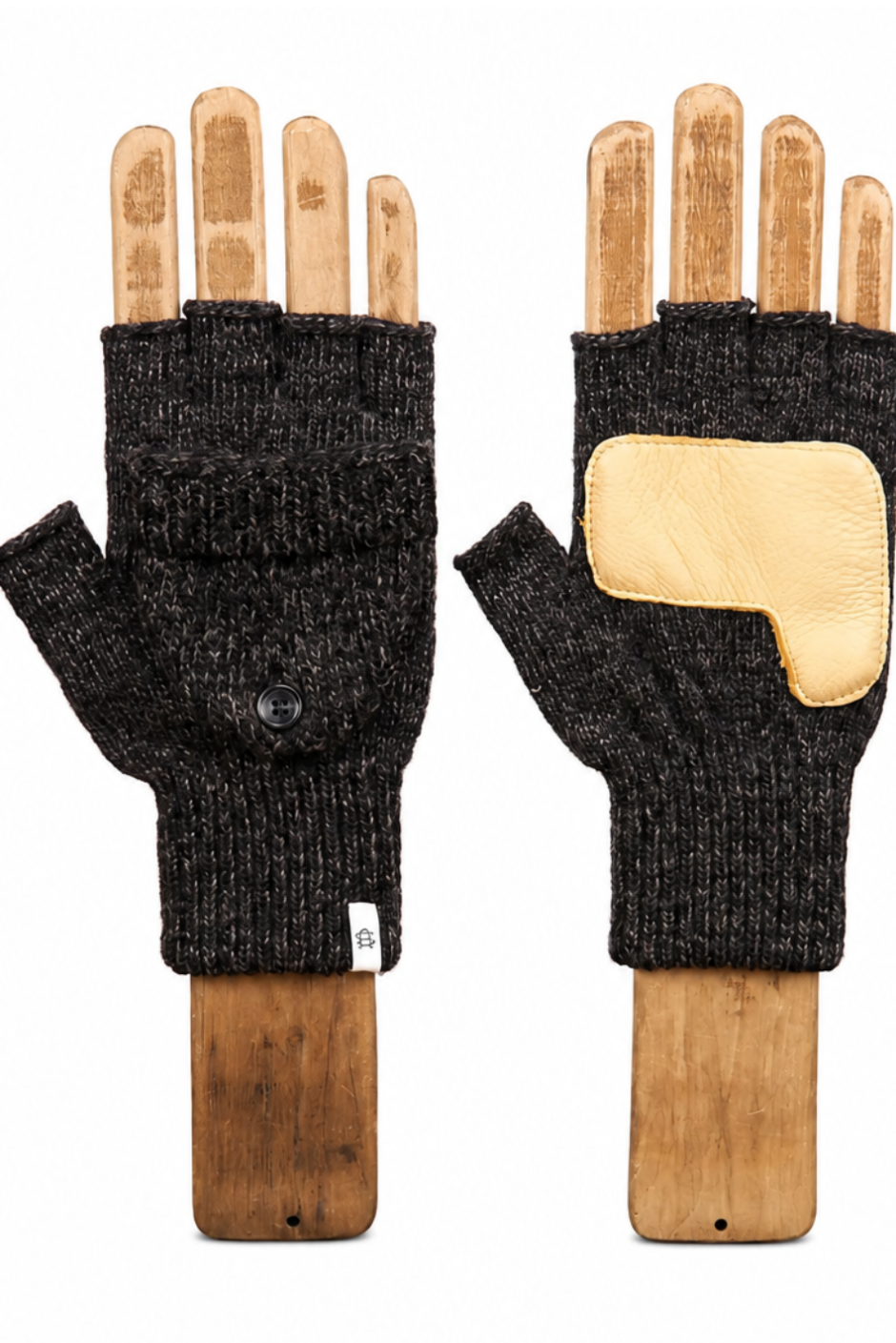 A pair of black fingerless knit gloves displayed on wooden hand-shaped mannequins against a plain white background. One glove shows the black ribbed knit body with a small metal snap button, and the other shows a light tan leather patch on the back of the hand.