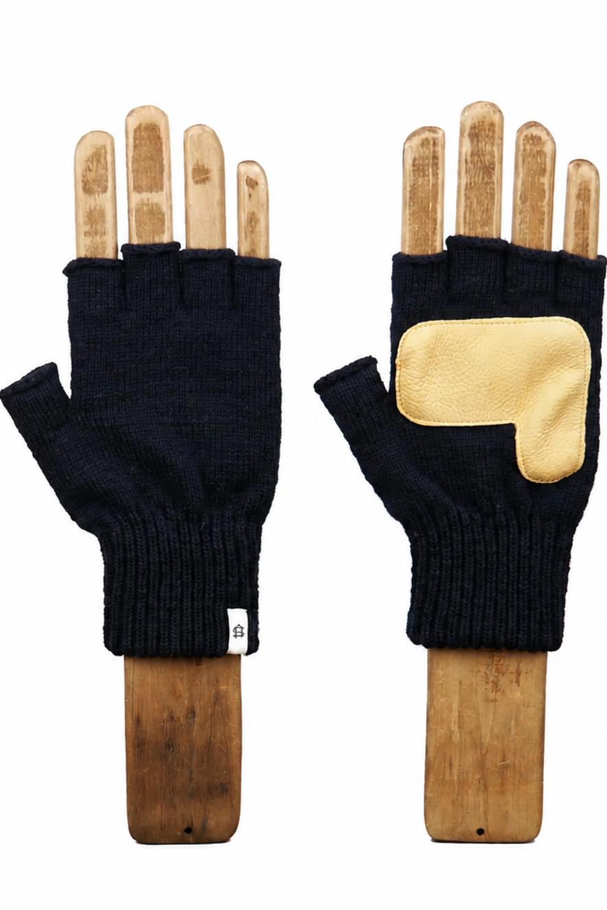 A pair of black fingerless knit gloves displayed on wooden hand forms against a plain white background. One glove is shown palm-side with a ribbed cuff and a small white tag, and the other is shown back-side with a large light beige patch on the back of the hand.