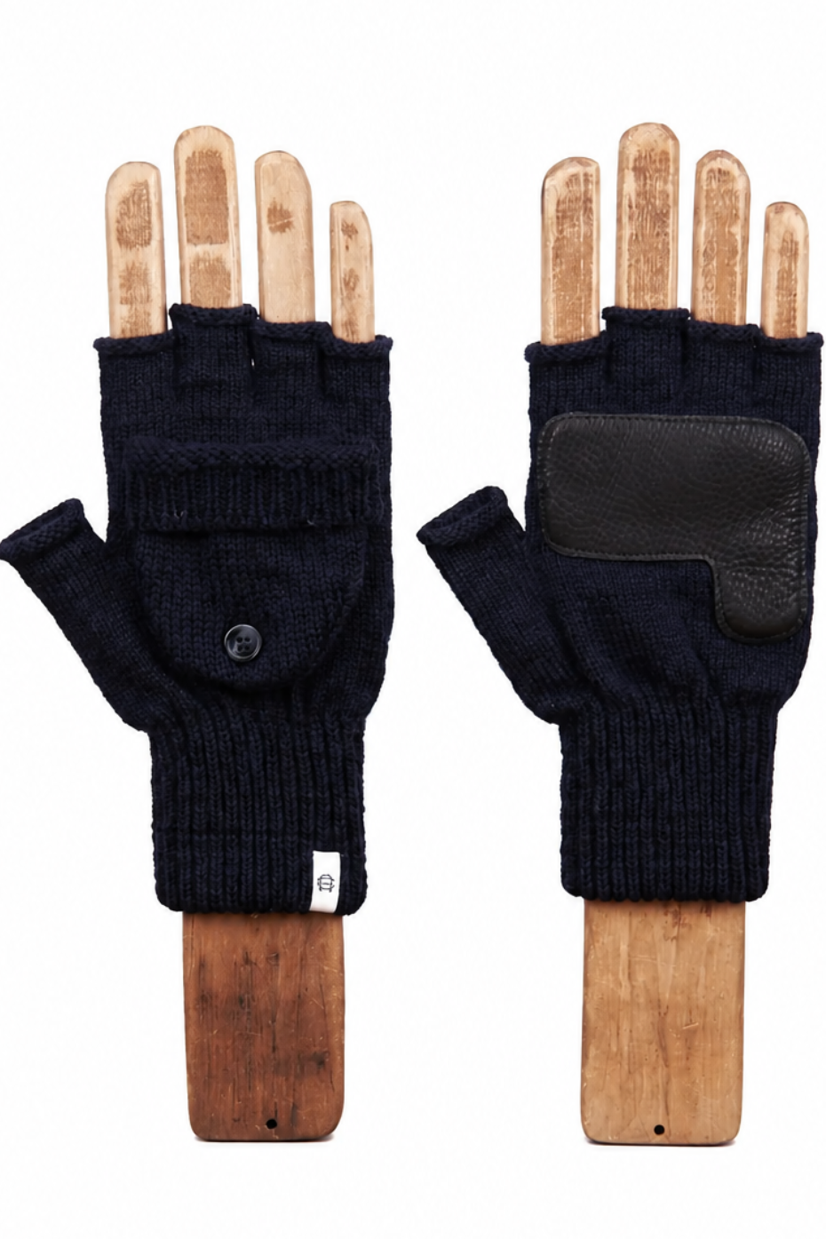 A pair of dark navy fingerless knit gloves displayed on wooden hand forms against a plain white background. One glove is shown from the palm side with a snap button, and the other shows the back with a black leather patch.