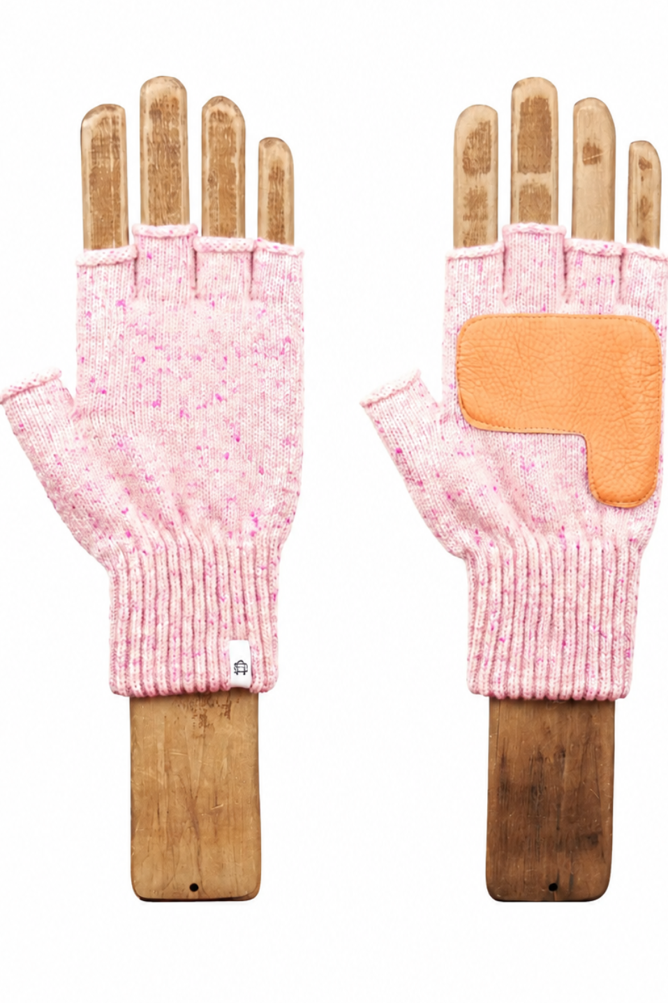 A pair of pink knit fingerless gloves displayed on wooden hand forms against a white background. One glove is shown from the back, featuring a textured pink knit body and a contrasting orange palm patch.