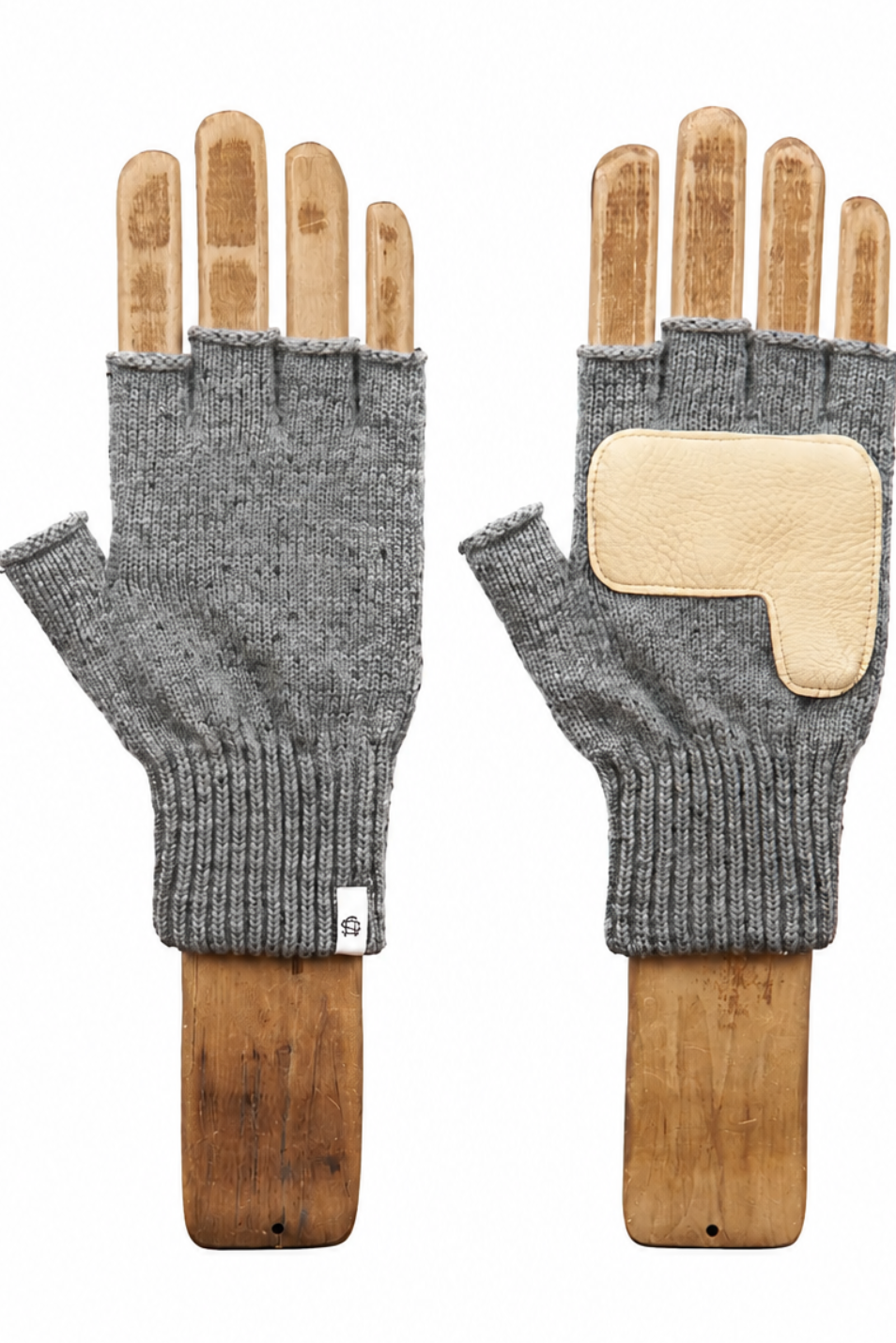 A pair of gray fingerless knit gloves displayed on wooden hand forms against a plain white background. One glove shows the knit palm side with a small white tag, and the other shows the back with a light beige leather patch on the back of the hand.