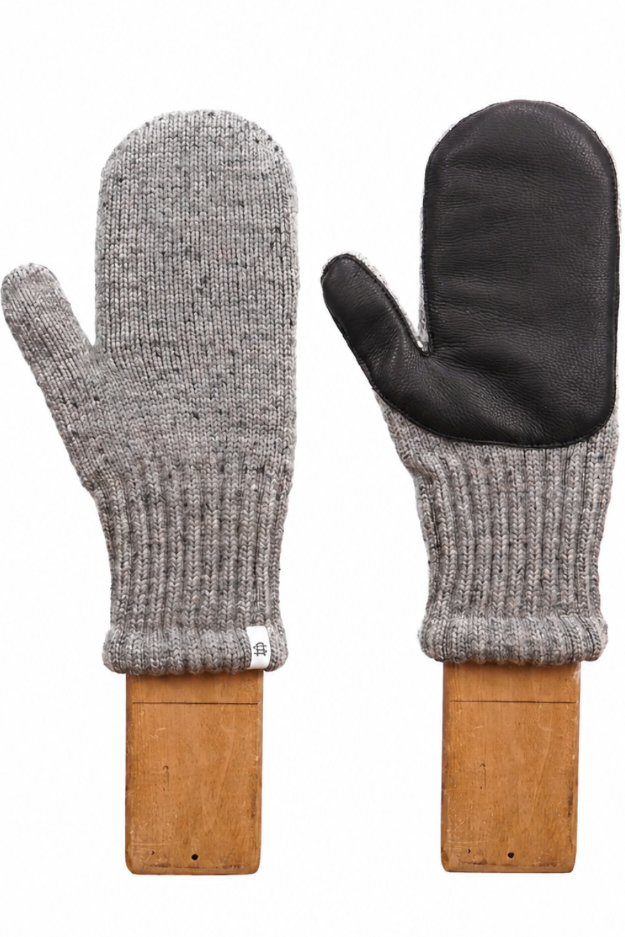 A pair of knit winter mittens displayed side by side on wooden stands against a plain white background. One mitten is shown from the back, featuring a heather gray ribbed knit body and a black leather palm.