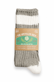 A single ribbed knit sock in heather gray and off-white, wrapped with a brown paper label that reads 'THE UPCYCLED SOCK' and '100% UPCYCLED COTTON'.