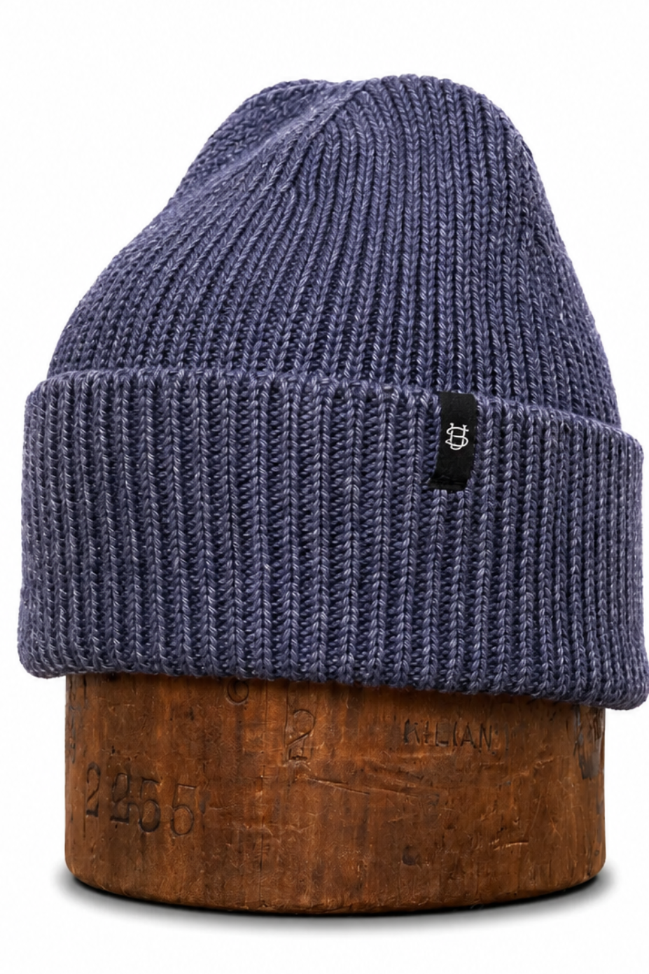 A ribbed knit beanie hat in a heathered slate blue color, displayed on a brown wooden stand against a plain white background.