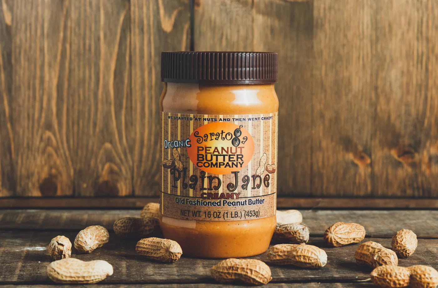 Jar of peanut butter with peanuts on a wooden surface